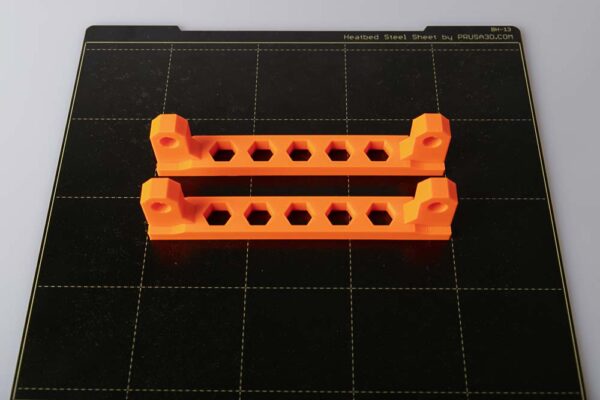 Printing plate of the Prusa i3 MK3S on which two orange 3D printed filament spool holders are placed. Details: Layer height 0.2 mm and Prusament PETG Prusa Orange
