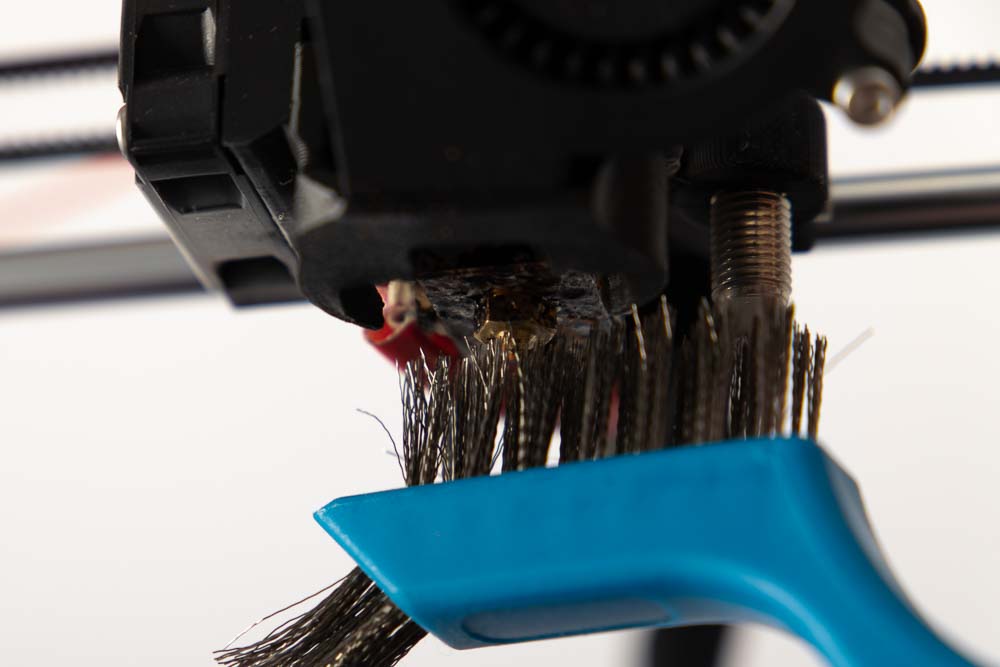 Cleaning dirty 3D printer nozzle with wire brush