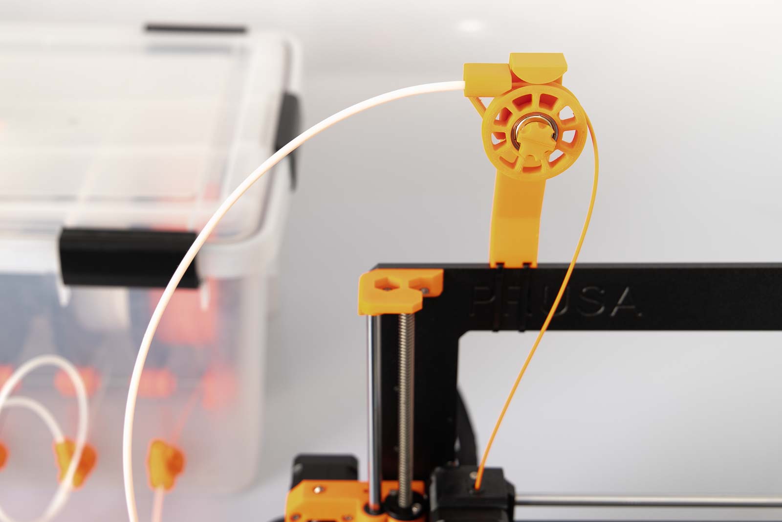 Filament guide with pulley mounted on the 3D printer with filament box in the background