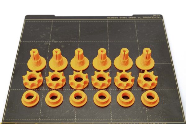 Printing plate of the Prusa i3 MK3S on which there are 6 pieces of 3D printed filament outlets, nuts, and clamping rings. All parts are printed in orange PETG filament with a layer height of 0.2 mm.