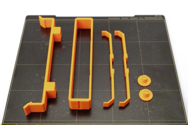 Print plate of the Prusa i3 MK3S on which there is a 3D printed bracket H12, two screws, a silica gel bag holder and two side supports. The 3D printed parts were printed in orange PETG filament with a layer height of 0.2 mm.