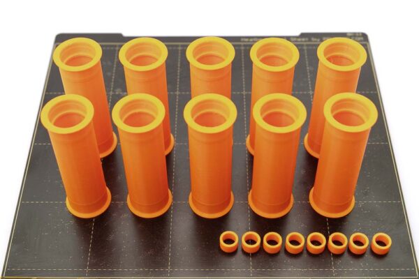 Build plate of the Prusa i3 MK3S on which there are 10 pieces of 3D printed wide pulleys with a width of 80 mm and 8 pieces of 3D printed spacers. All parts are printed in orange PETG filament.