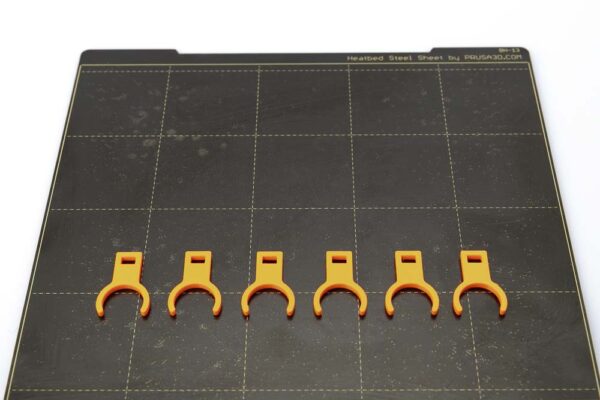 Print plate of the Prusa i3 MK3S on which 6 clips variant A lie. The clips were printed in orange PETG filament with a layer height of 0.2 mm.