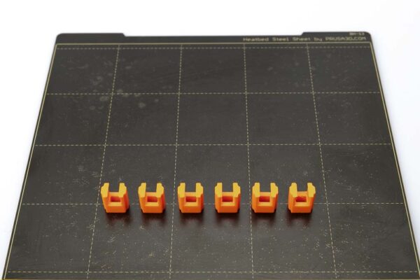 Print plate of the Prusa i3 MK3S on which 6 clips variant B lie. The clips were printed in orange PETG filament with a layer height of 0.2 mm.