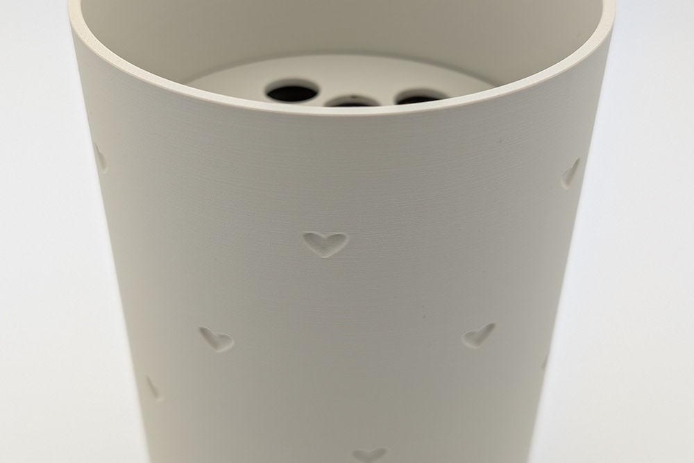 Beige 3D-printed flower vase featuring debossed mini hearts and a visible flower frog insert.