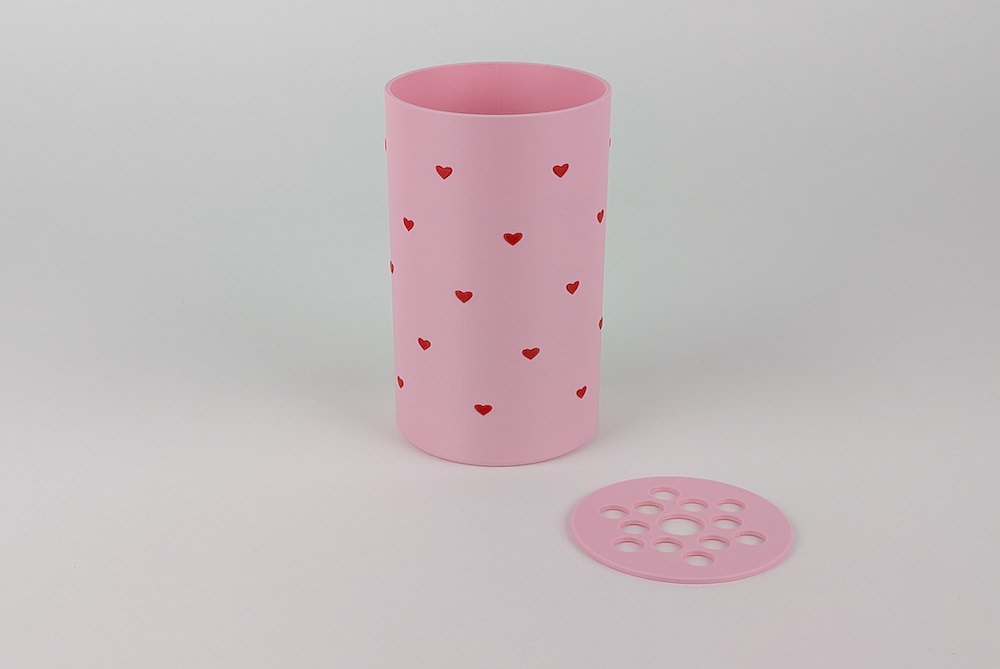 3D printed vase, printed in pink filament. The hearts are red and embossed, and you can see the flower disc right next to it.