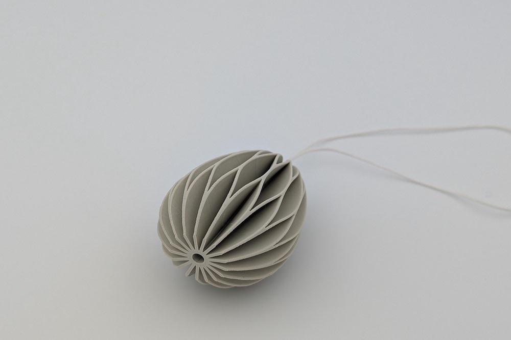 Close-up of a beige 3D-printed Easter egg with a string, viewed from below